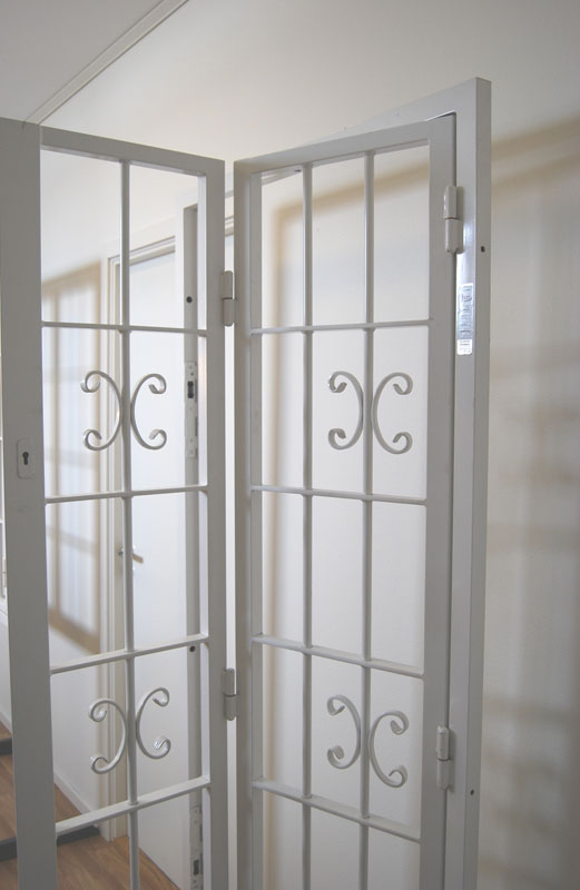 Vikbar dekorativ gallergrind i vit färg framför dörr